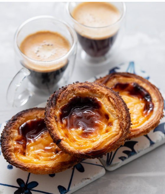 Une assiette de pastéis de nata avec une tasse de café en arrière-plan.