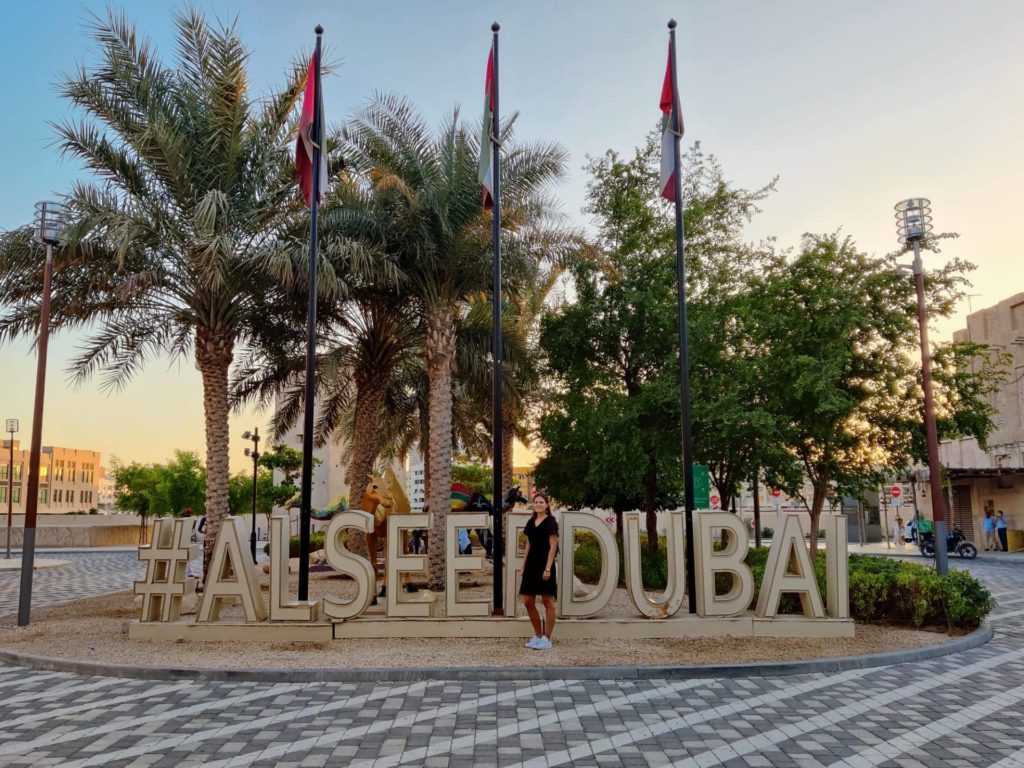 posing in front of al seef district letters